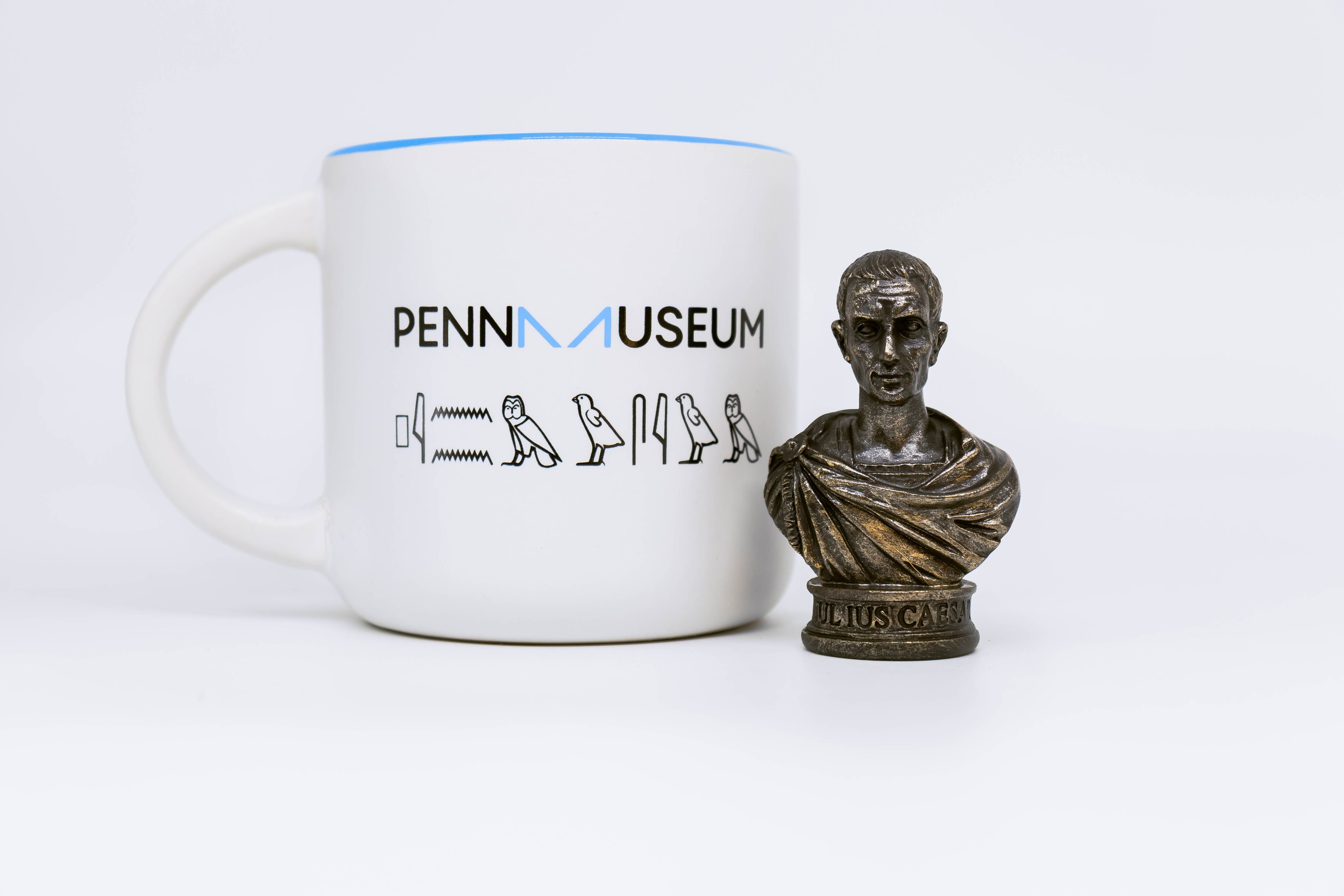 Caesar bust displayed next to white mug with Penn museum logo and hieroglyphs underneath logo. 