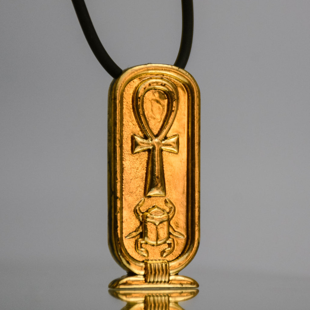 Cartouche pendant with reflection and on black necklace, gray background. 