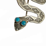 Close up of the head of a silver snake brooch with turquoise stones for eyes on a white background