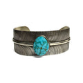 Front view of a silver bracelet with feather pattern and large turquoise stone at the center on a white background.