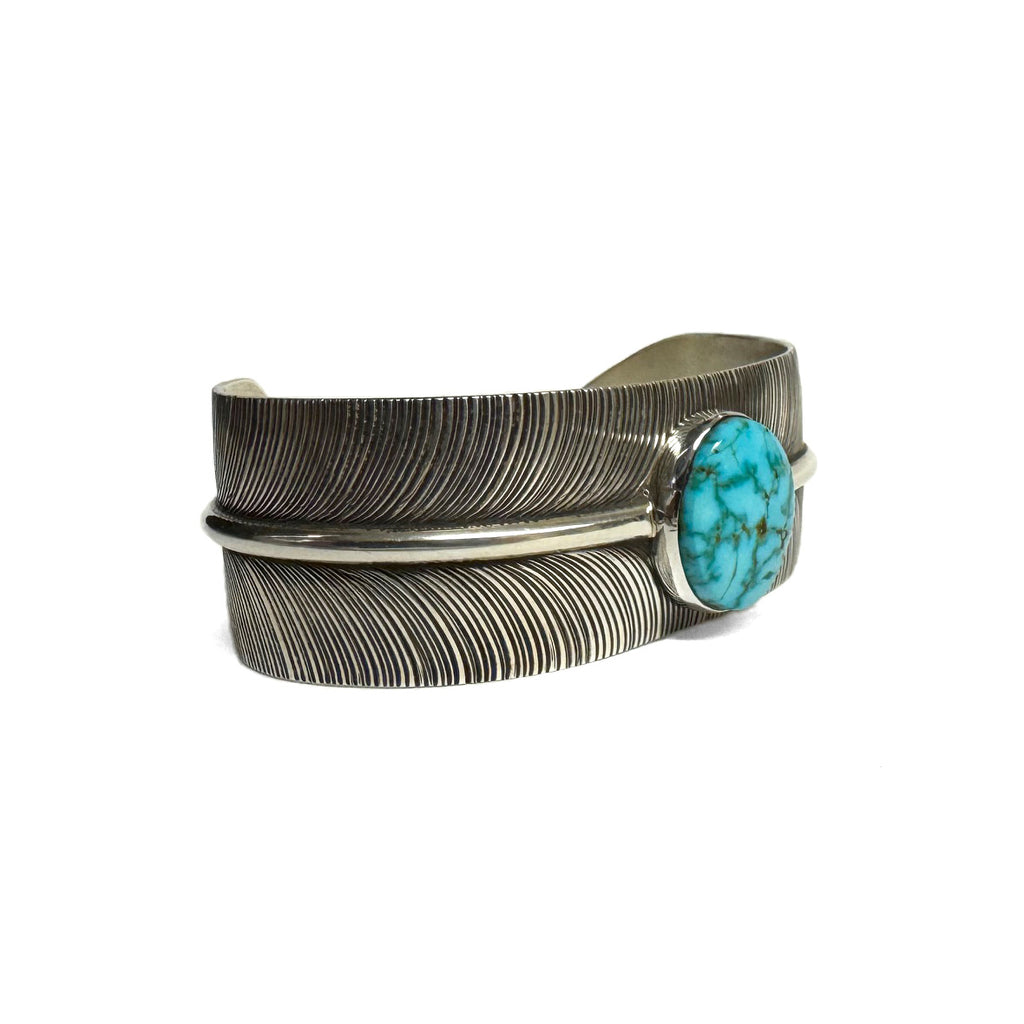 3/4 view of a silver bracelet with feather pattern and large turquoise stone at the center (facing right) on a white background.