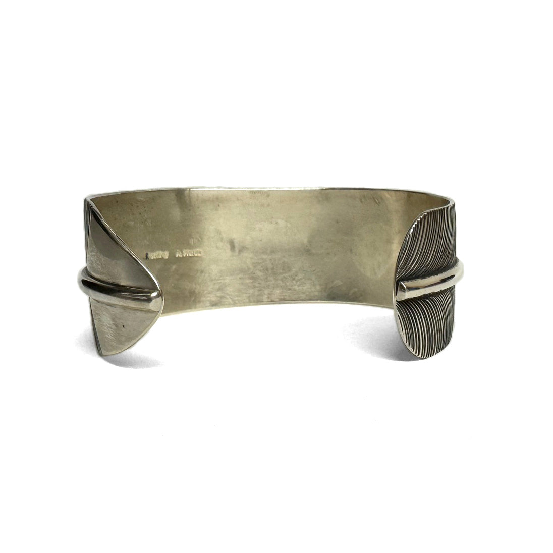 Back (inside) view of a silver bracelet with feather pattern on a white background.