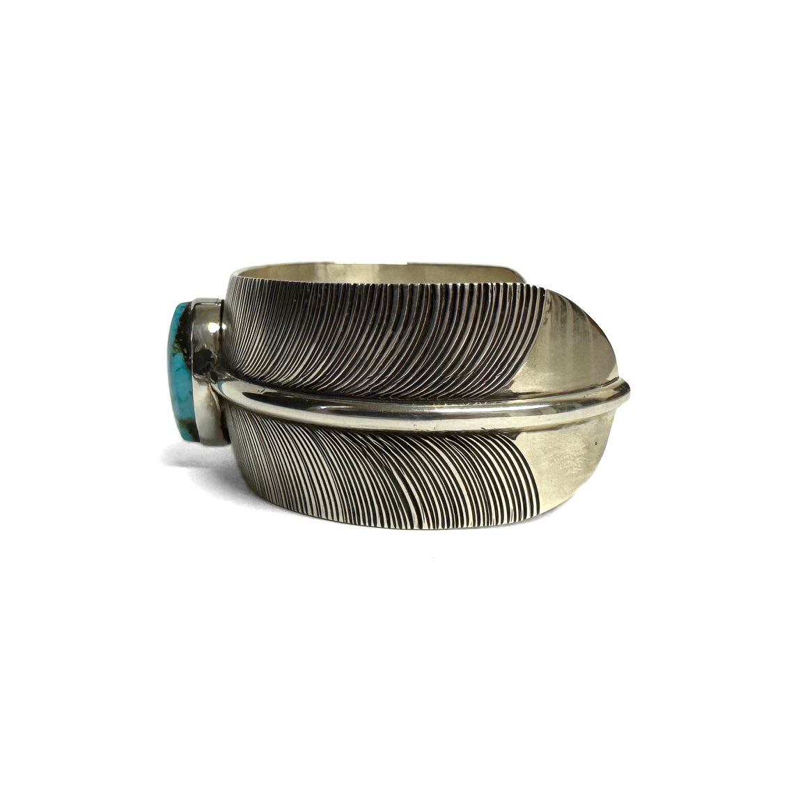 Side view of a silver bracelet with feather pattern and large turquoise stone at the center (facing left) on a white background.