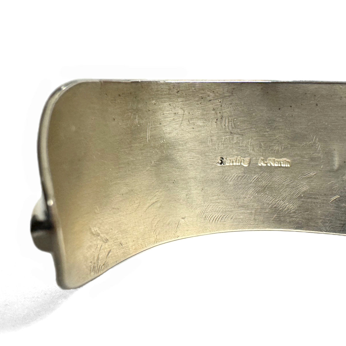 Close up of the inside of silver bracelet showing stamp of "Sterling Silver" and the artist signature "A. Martin" on a white background.