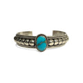 Front view of a silver bracelet featuring artistic accents and a turquoise stone at the center. Turquoise stone has a natural vein running through the center. Bracelet is on a white background.