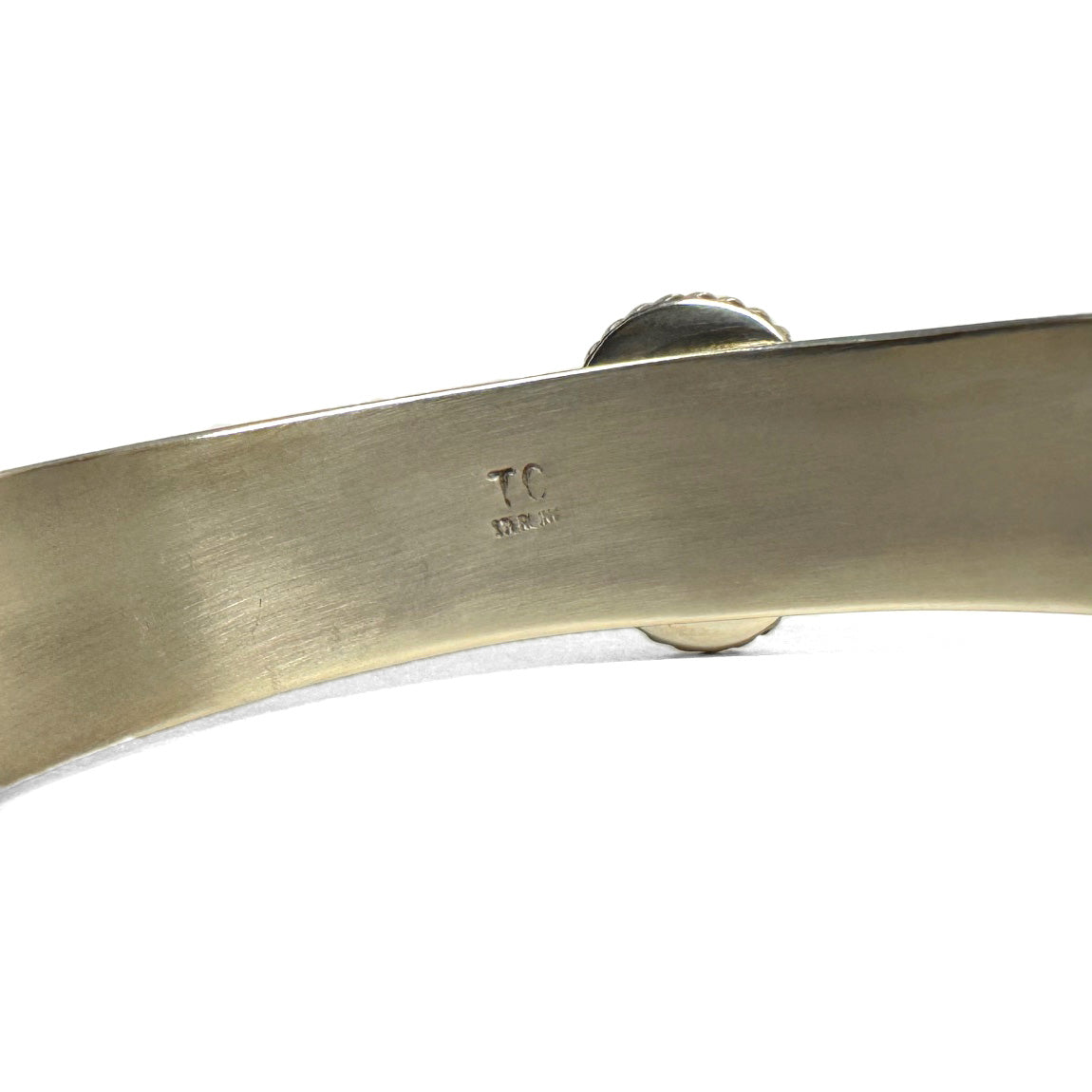 Close up of the inside of a silver bracelet showing the stamp "sterling silver" and the artists signature TC, for Thomas Charley.