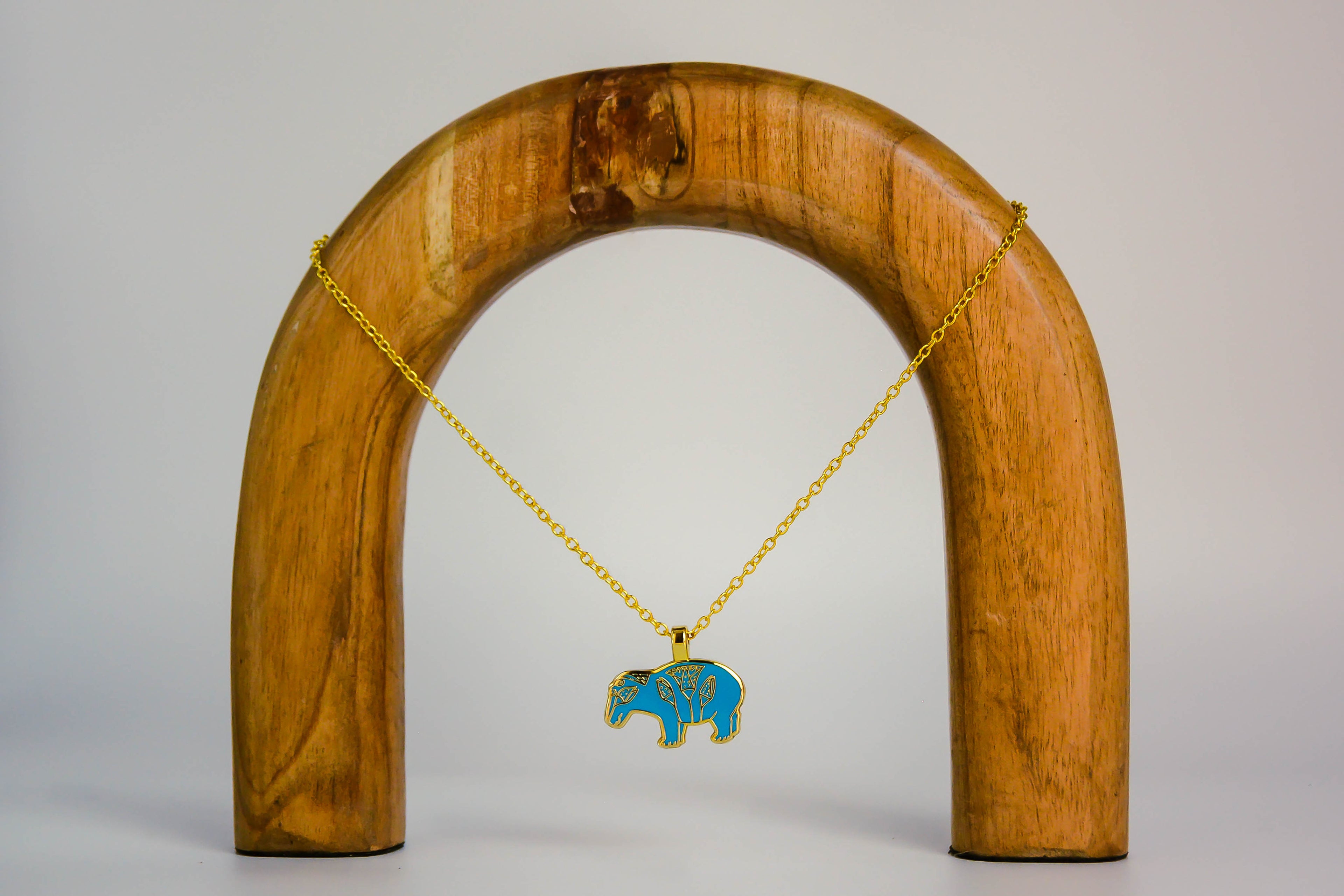 Hippo necklace on a wooden arch, on off-white background. 
