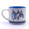 A ceramic mug with blue and white design featuring a graphic of orcas.